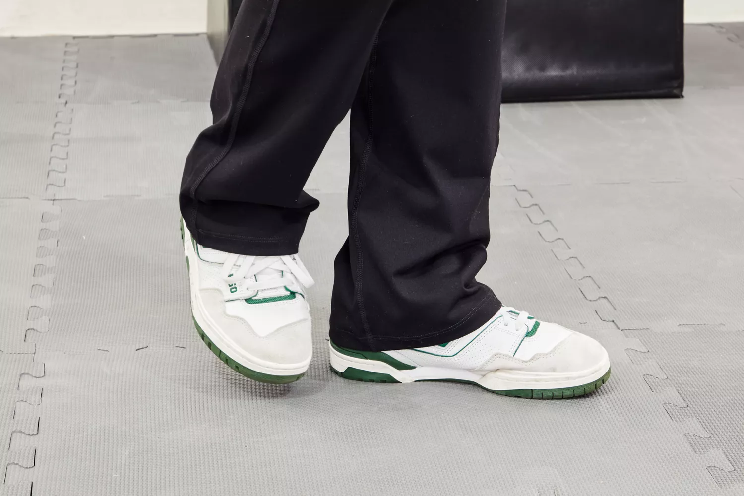 Close up of a person's lower legs in black athletic pants and sneakers on gym mats.