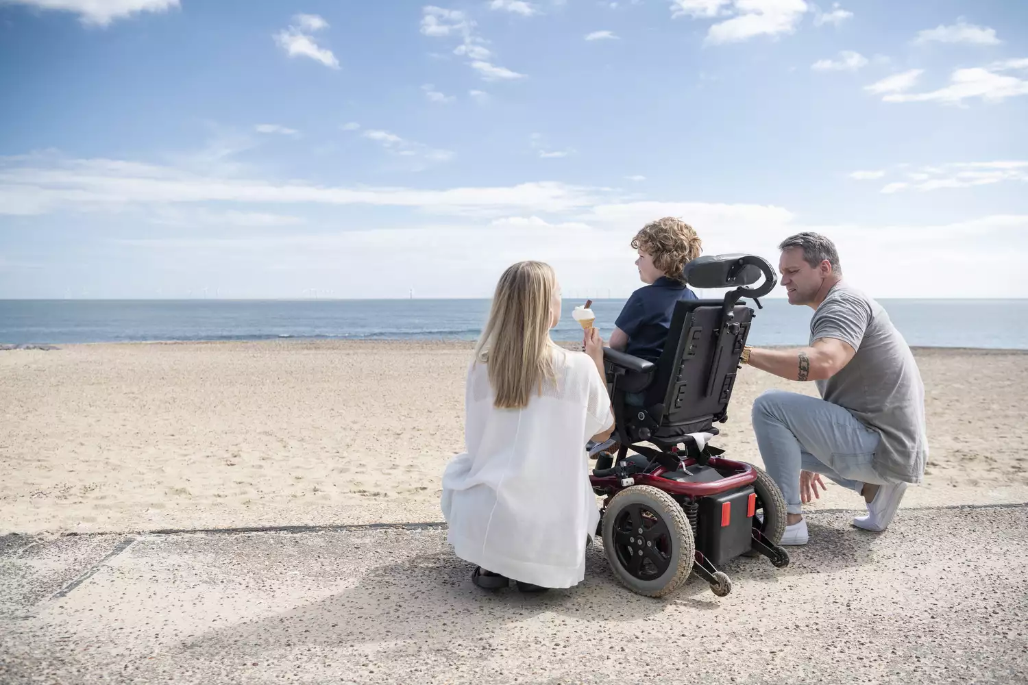 A family at the beach with a child in a power wheelchair enjoying a sunny day.