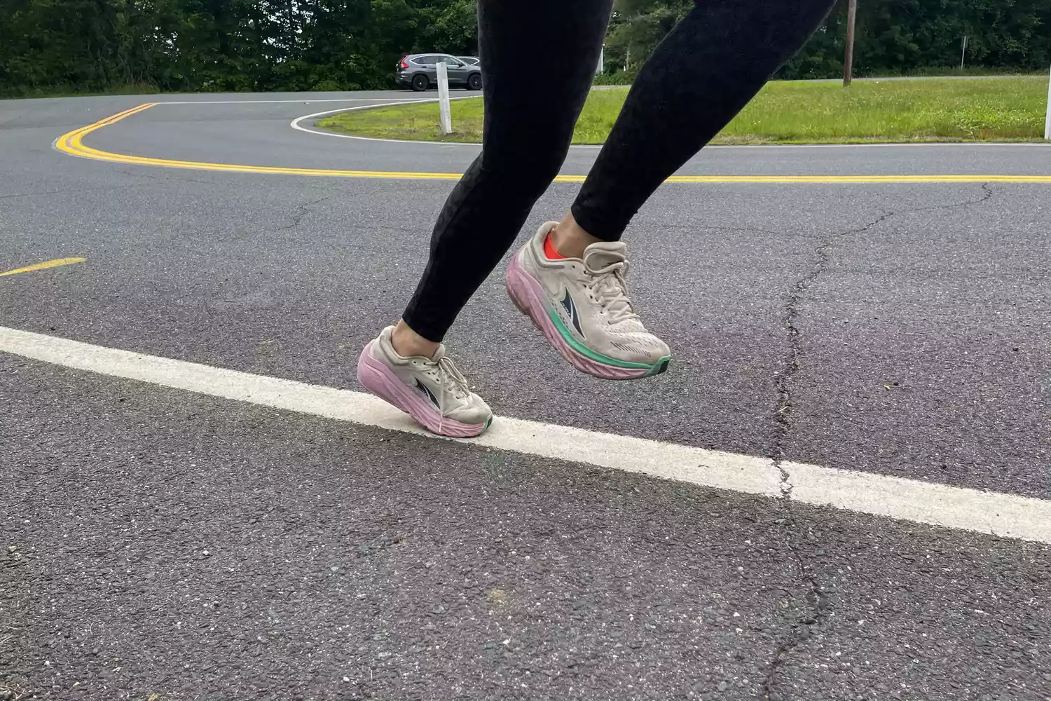 A runner's legs captured mid-stride on a paved road, demonstrating proper running form in low-drop shoes.