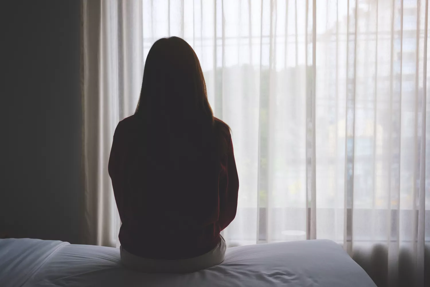 A silhouetted figure sitting on a bed by a window, evoking a sense of rest and recovery.