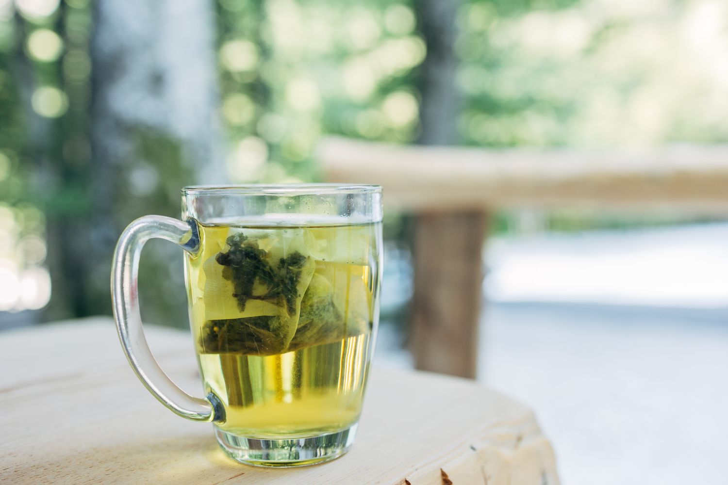 A clear mug of green tea on a minimalist surface.