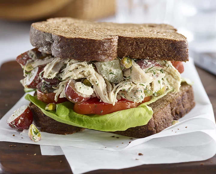 Southampton chicken salad with visible red potato skins and chopped pistachios in a white serving bowl.