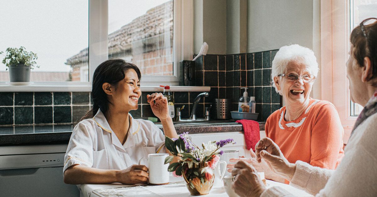 An attentive caregiver interacting with two seniors during tea time in a home setting.