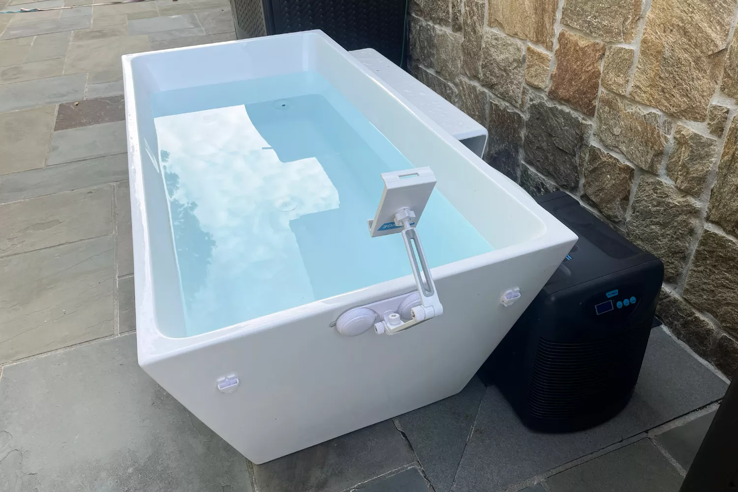 A white outdoor cold plunge tub with a digital thermometer and a dedicated cooling chiller.