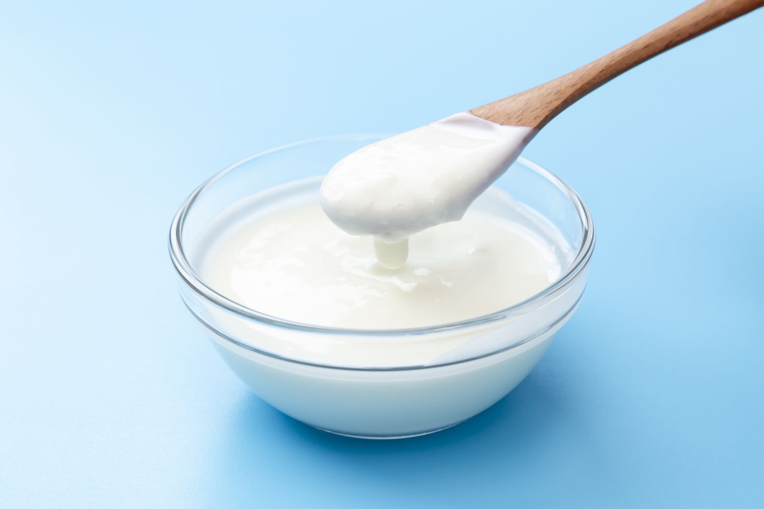 A white bowl filled with plain yogurt on a solid blue surface.