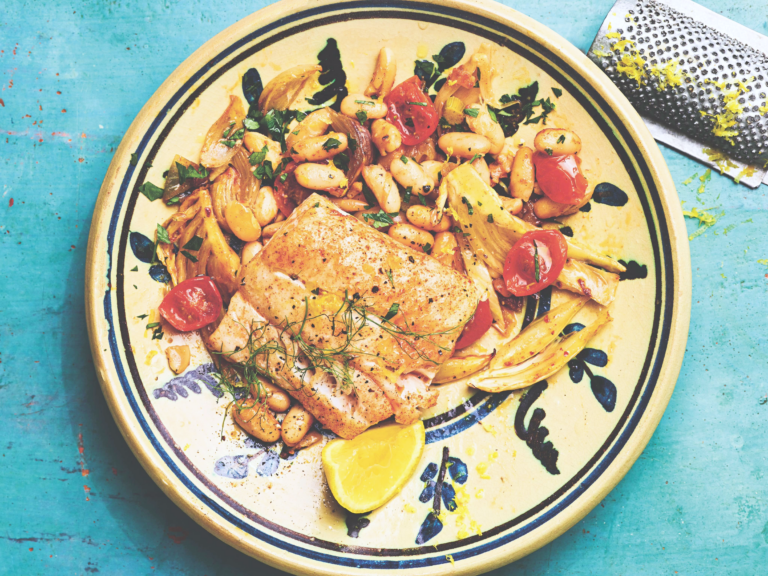 Close-up of baked haddock fillets with a smoky paprika rub served with caramelized fennel and cannellini beans.