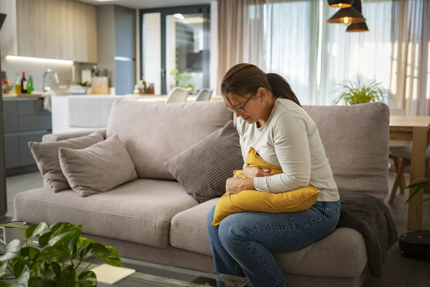 A person sitting on a sofa holding their stomach expressing physical discomfort.