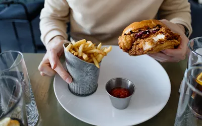 A fried chicken sandwich and fries on a plate, representing heavy meals that can trigger bloating.