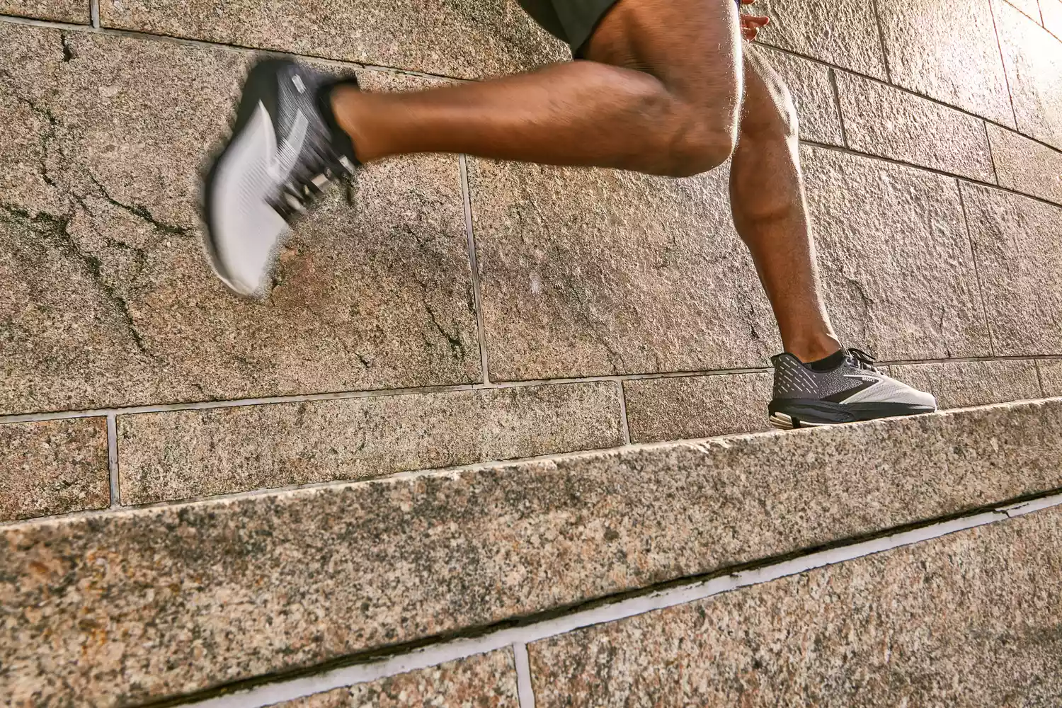 A runner wearing Brooks running shoes ascending stone steps during an outdoor workout.