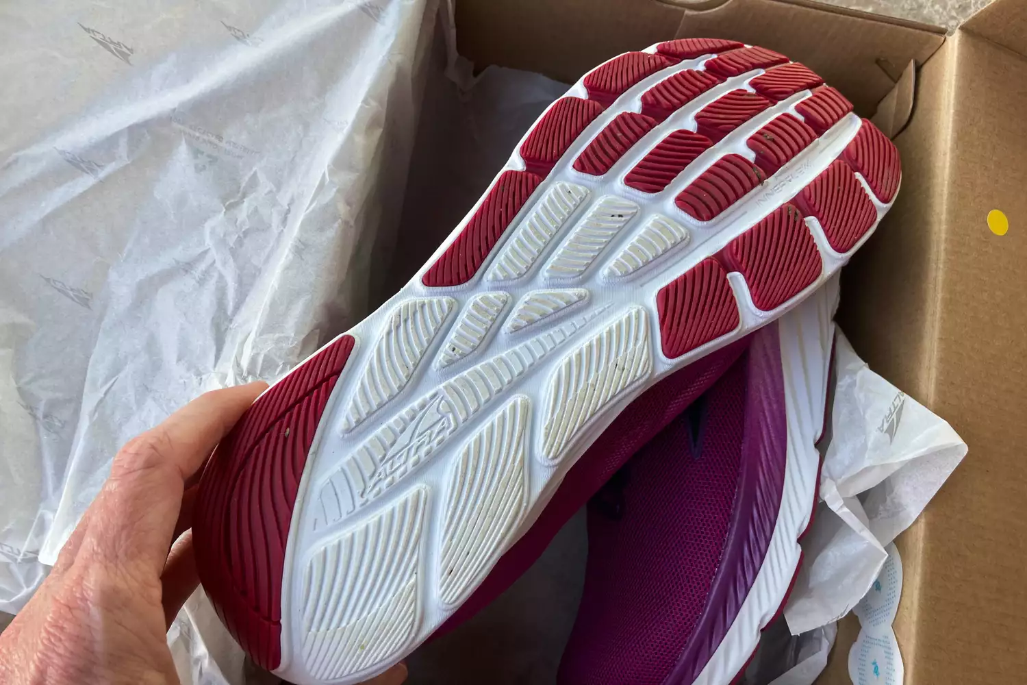 A hand holding up the sole of a new Altra shoe to show the red and white tread pattern.