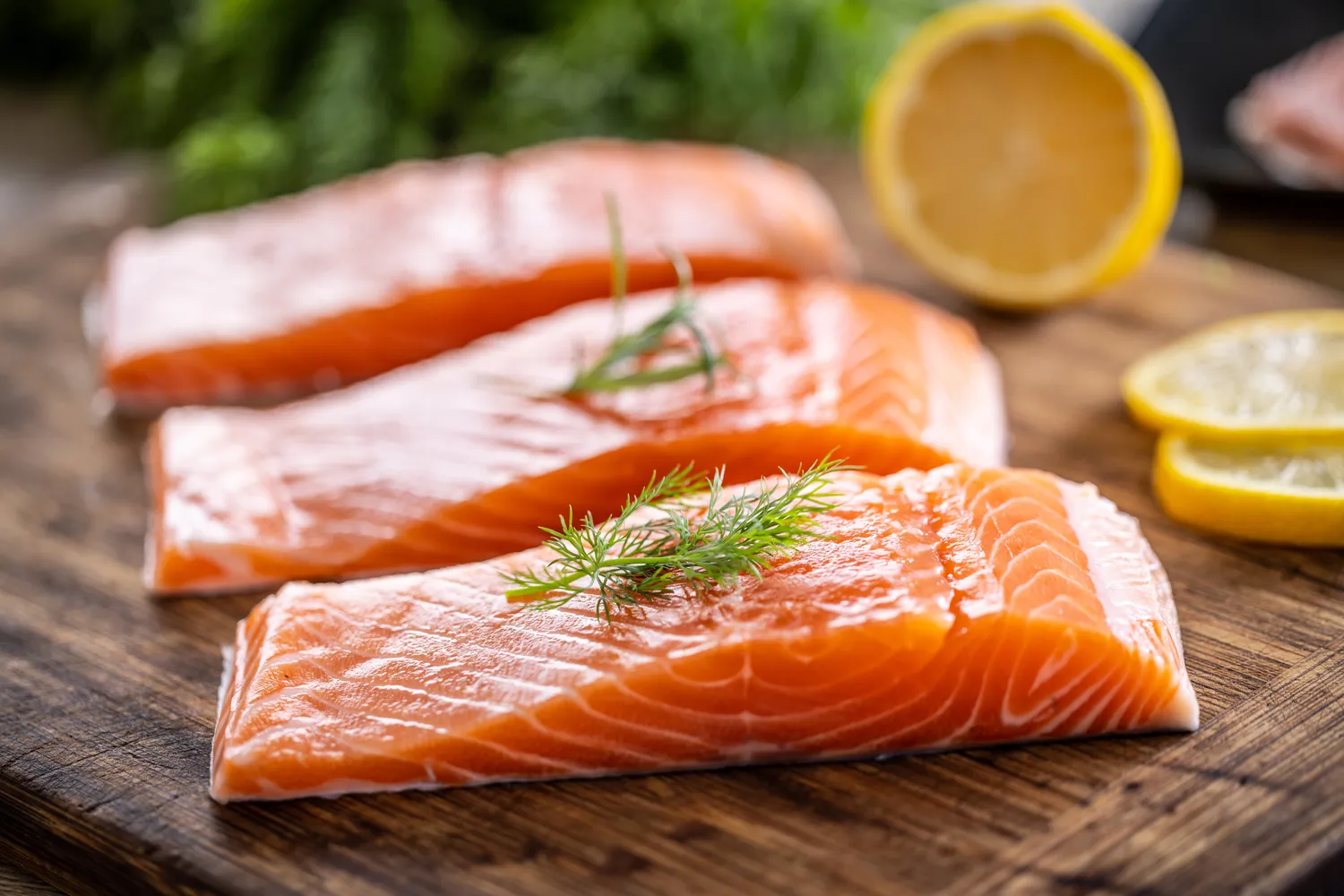 Fresh raw salmon fillets on a wooden board with dill and lemon.