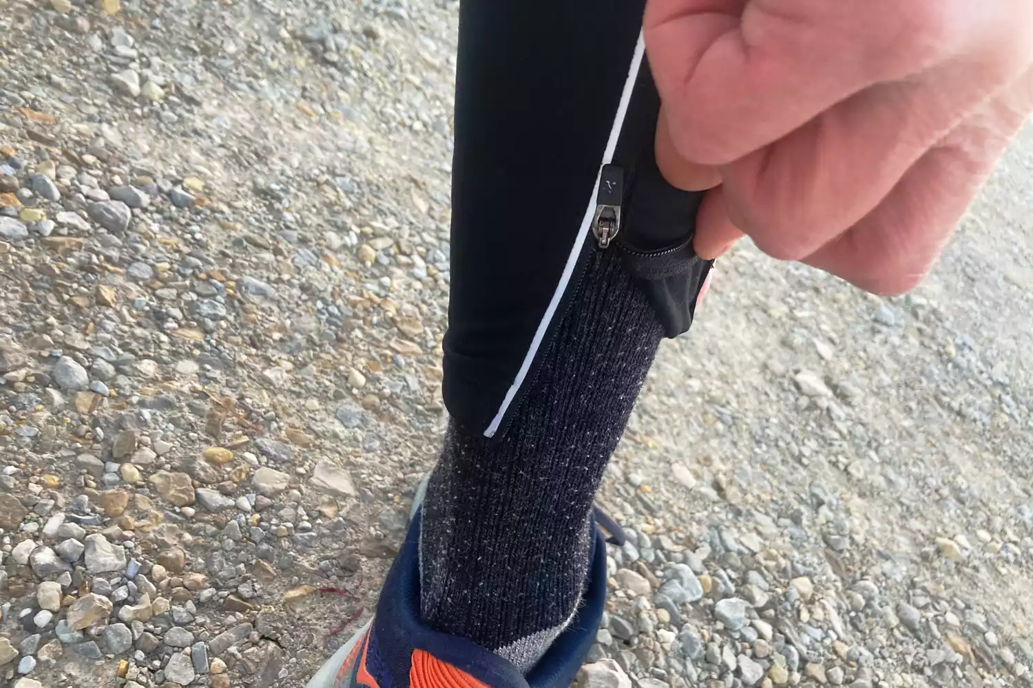 Close-up of a person adjusting an ankle zipper on black leggings over thick socks.