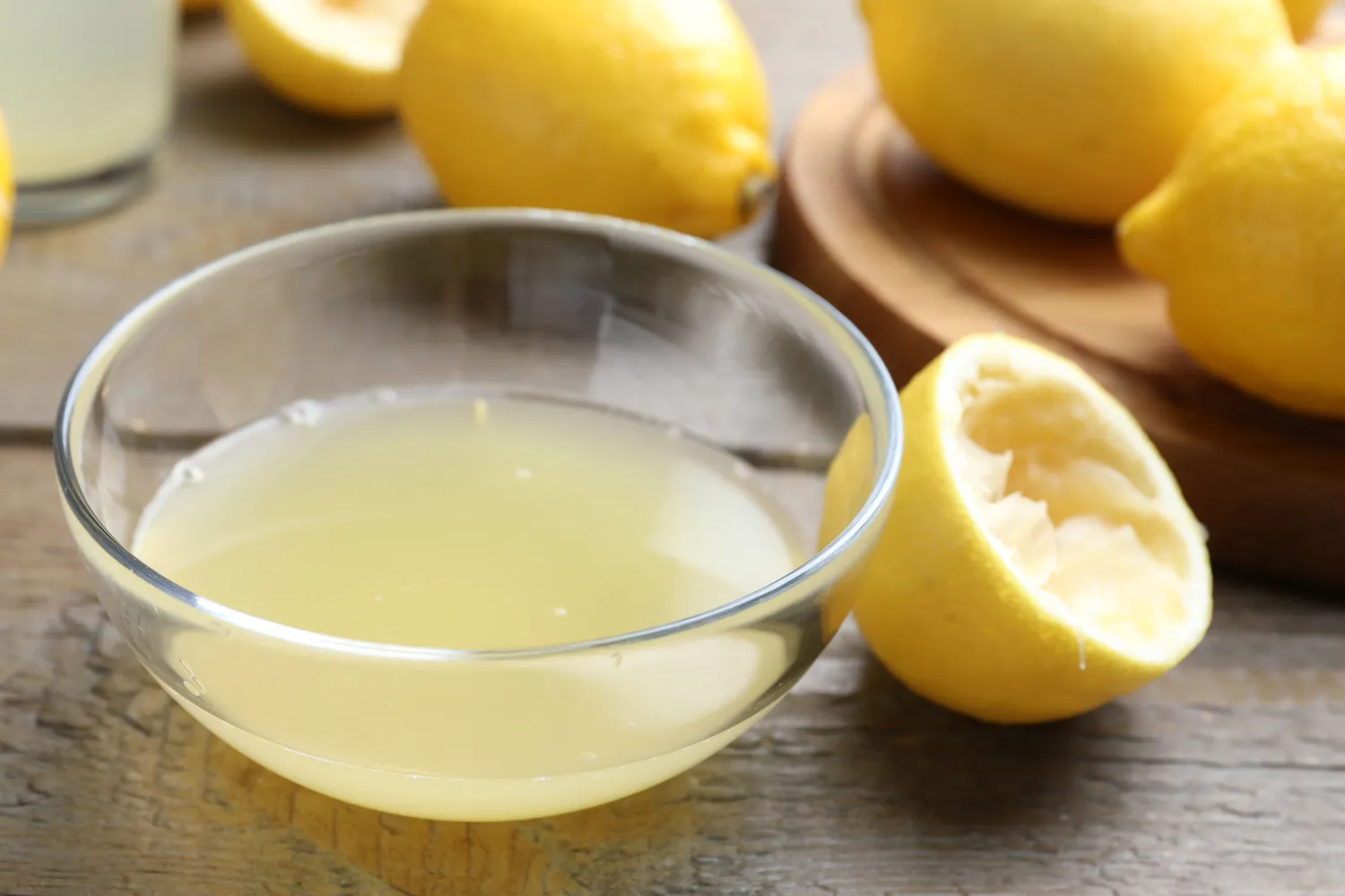 A bowl of freshly squeezed lemon juice next to cut lemon halves.