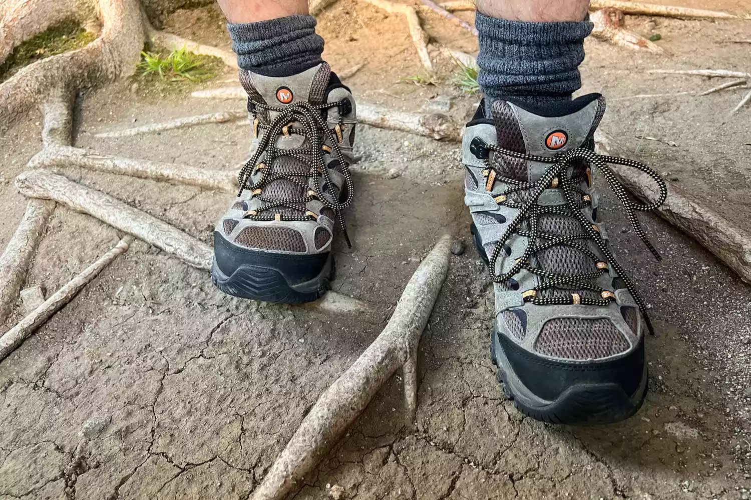 A hiker wearing Merrell Moab 3 Mid boots on a root-covered forest trail.