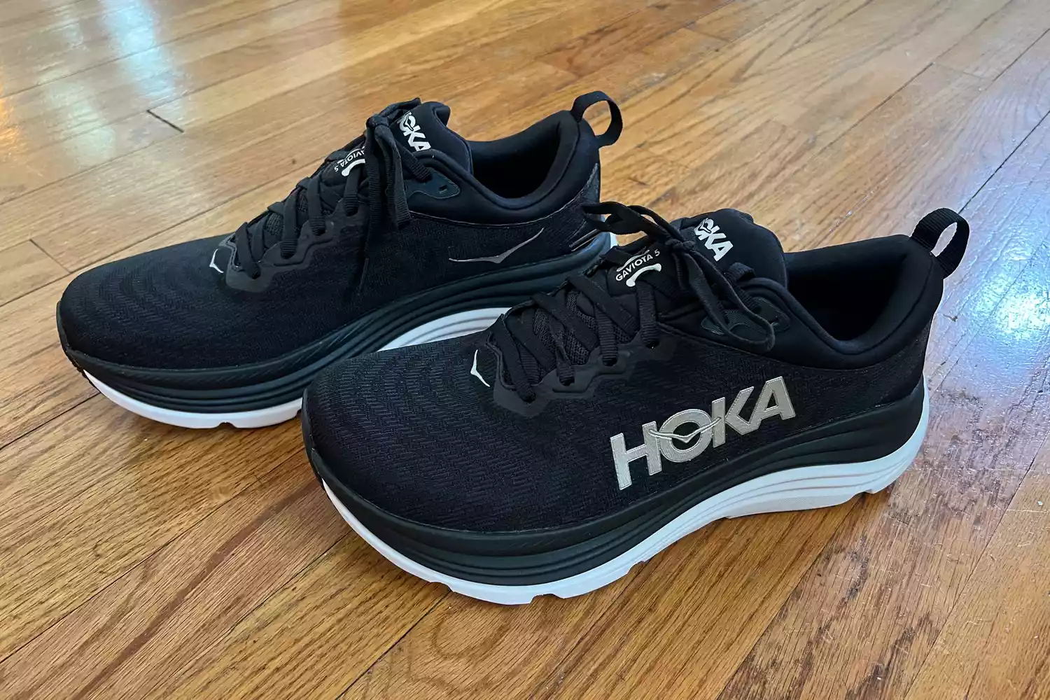 Black Hoka Gaviota 5 stability running shoes with white midsoles on a wooden floor.