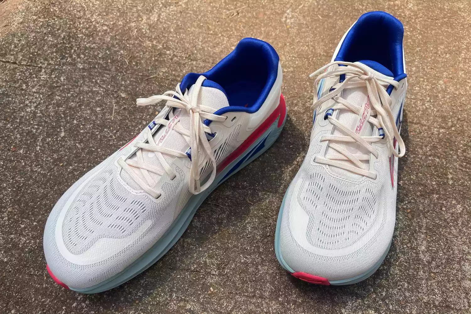 Side view of white Altra Paradigm 7 running shoes with blue and pink accents on a concrete surface.