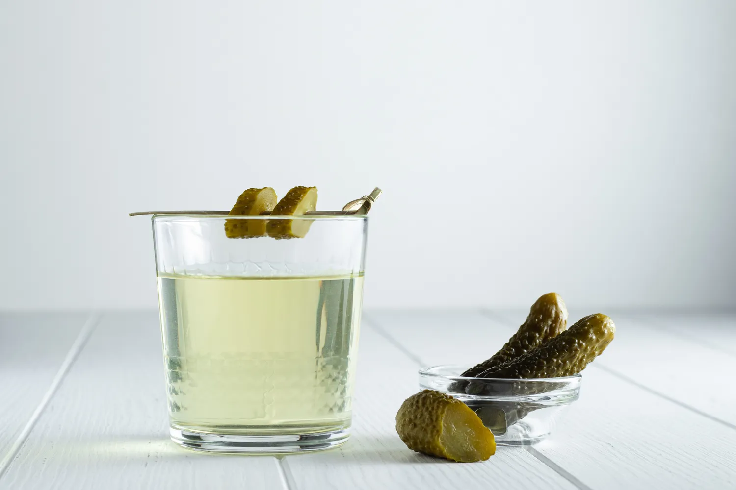 A glass of green pickle juice next to a jar of pickles.