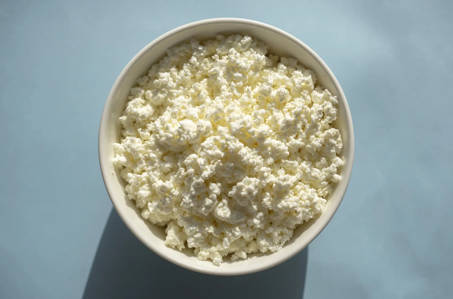 A bowl of cottage cheese showing its texture, placed on a neutral surface.