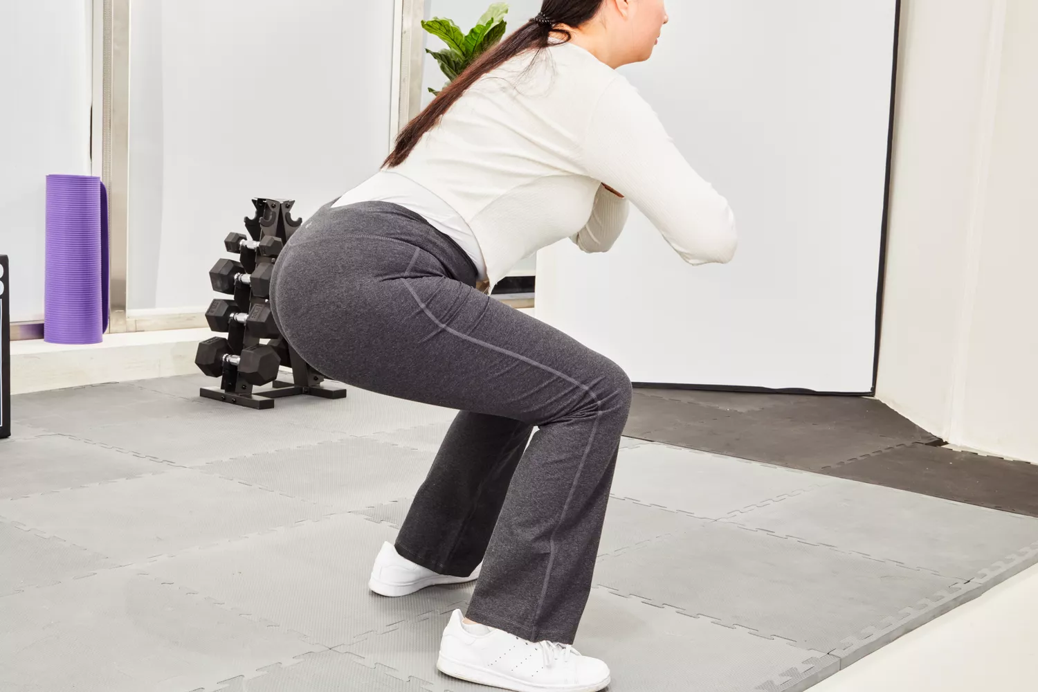 A woman performing a deep bodyweight squat in a home gym wearing black compression leggings.