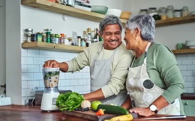 An older couple in a kitchen preparing a fresh vegetable smoothie together.
