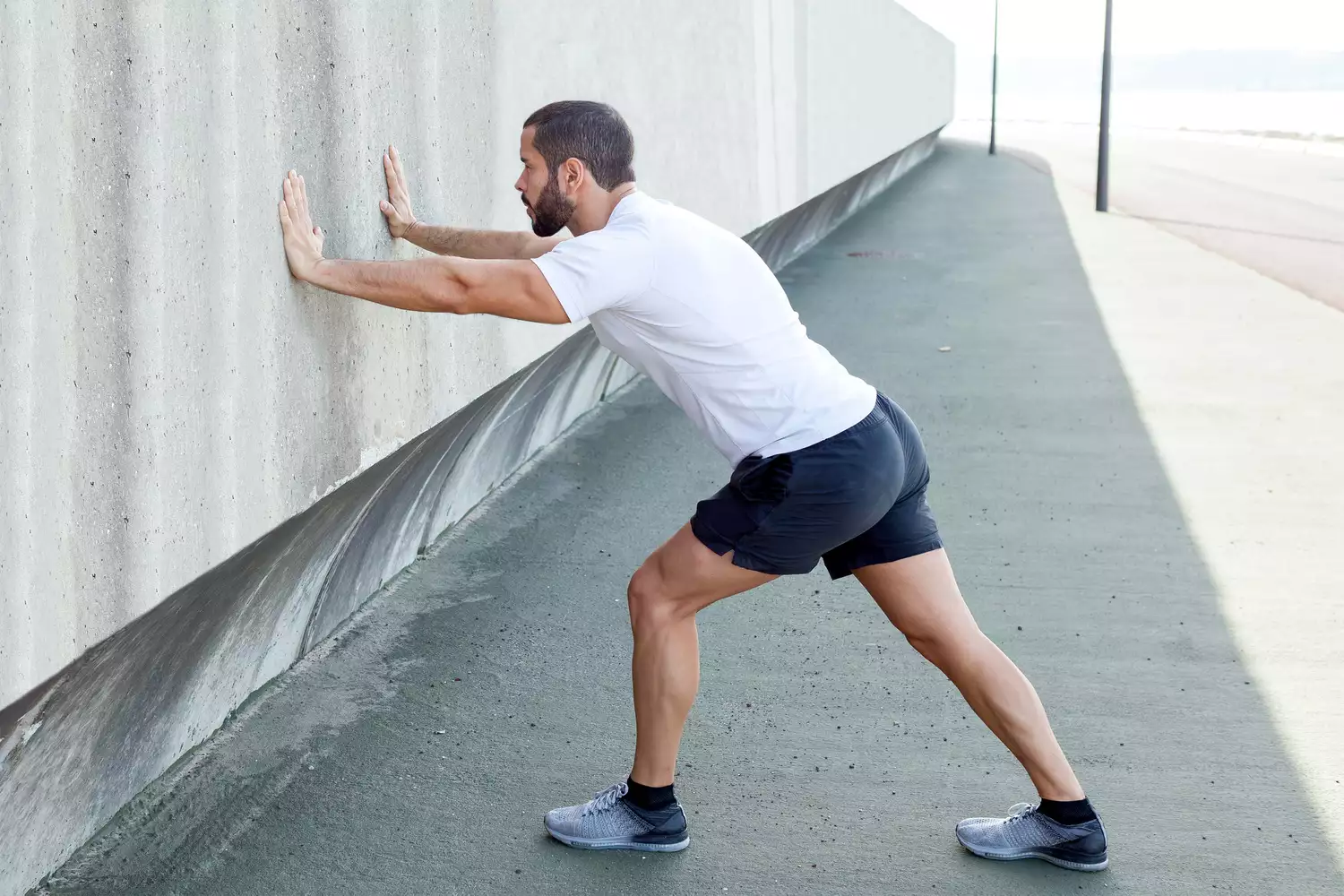 A man stretching his calf muscle against a wall.