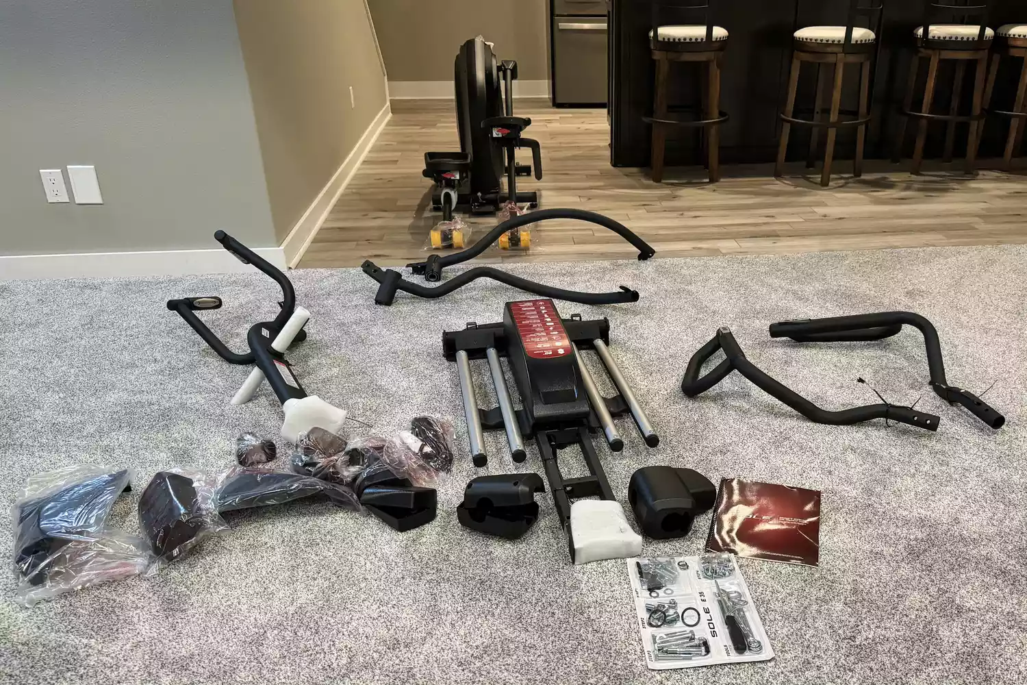 Disassembled parts of a Sole E35 elliptical trainer spread out on a carpet during assembly.