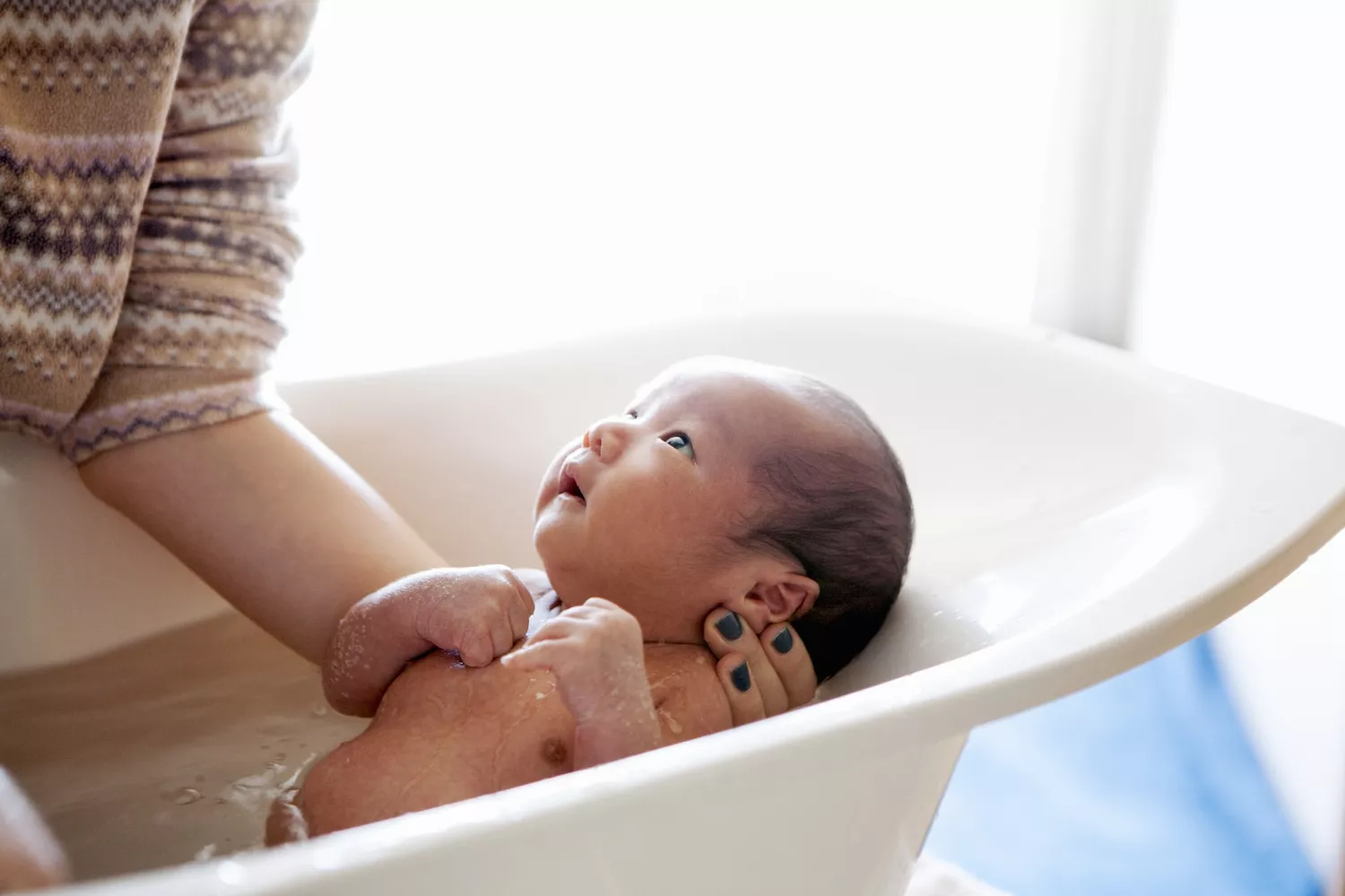 A woman bending over to wash a baby in a small bathtub, demonstrating daily lumbar usage.