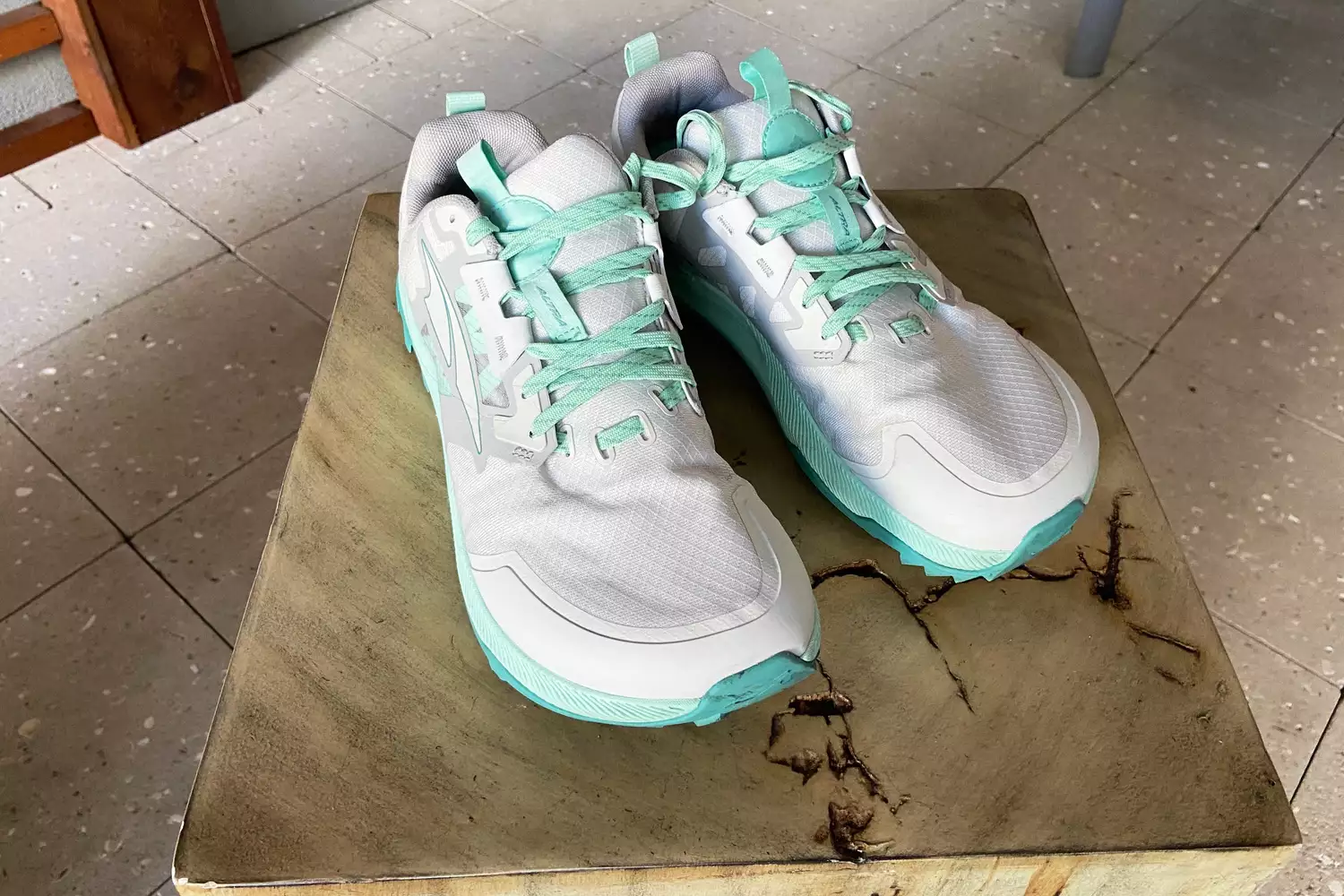 Altra Lone Peak 7 trail running shoes in white and mint green displayed on a wooden block.