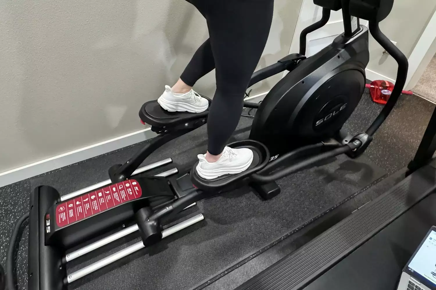 A person wearing leggings and sneakers exercising on a Sole E35 elliptical machine.