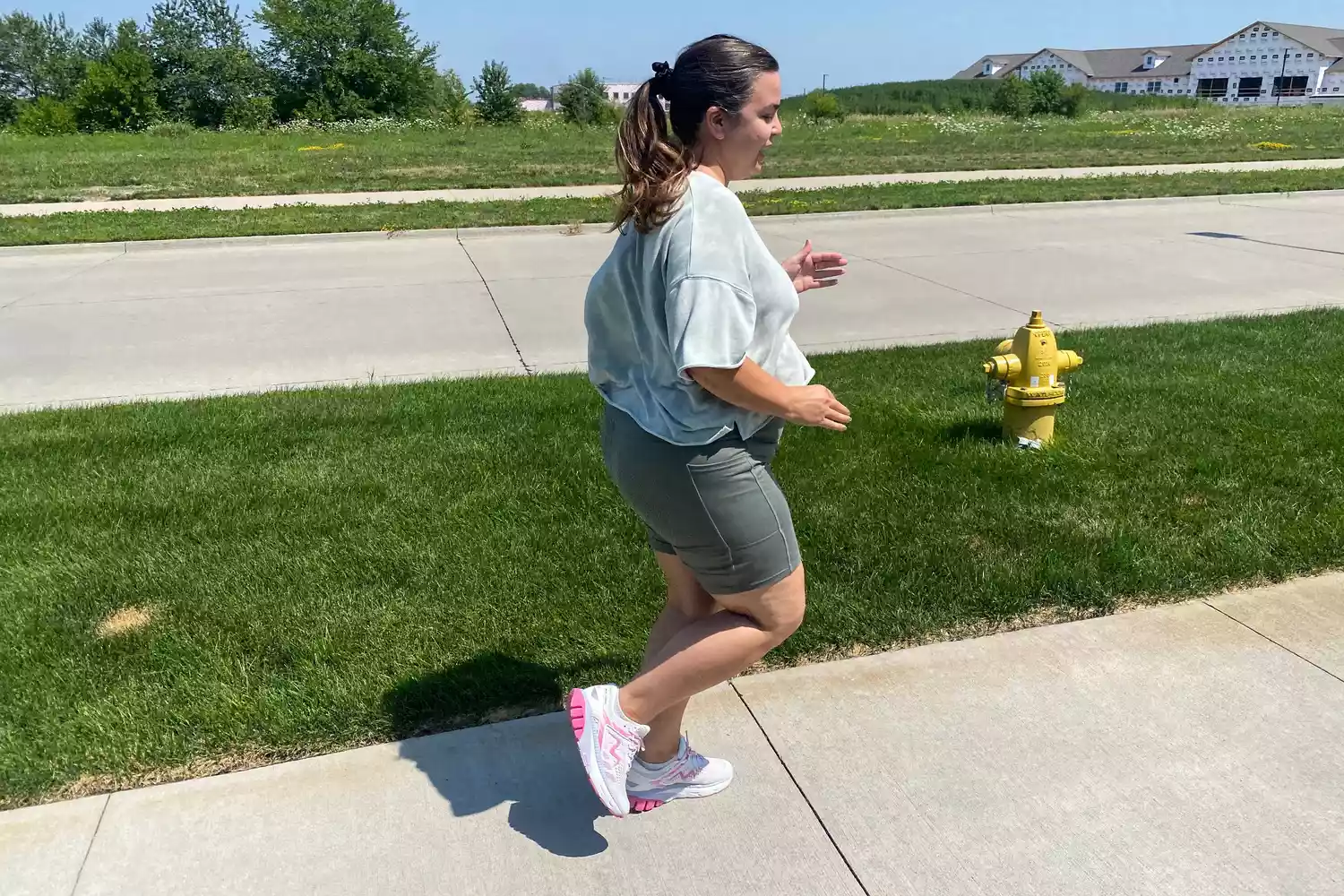 A woman jogging comfortably on a sunny suburban sidewalk wearing athletic gear.