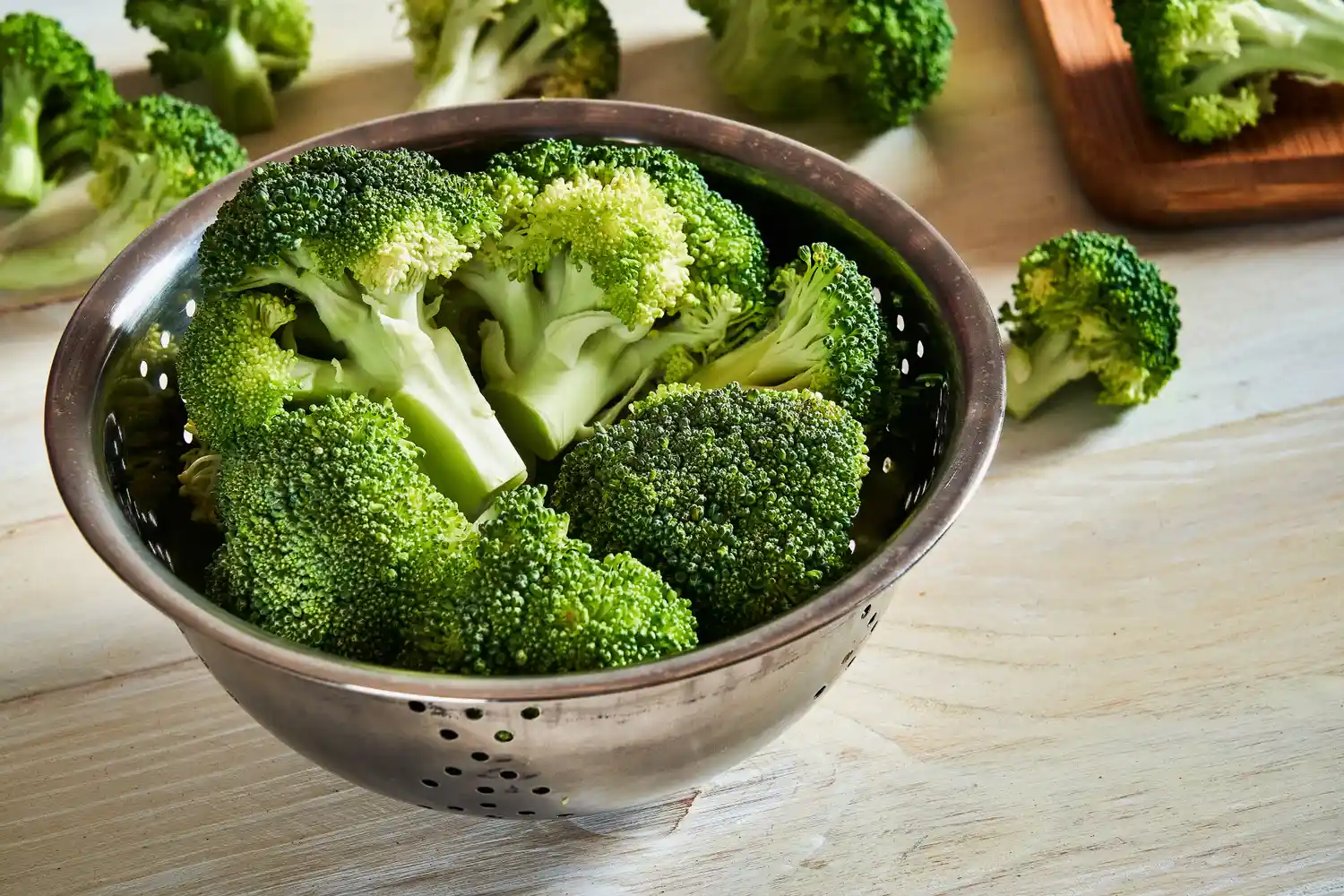 Fresh green broccoli florets in a metal colander.