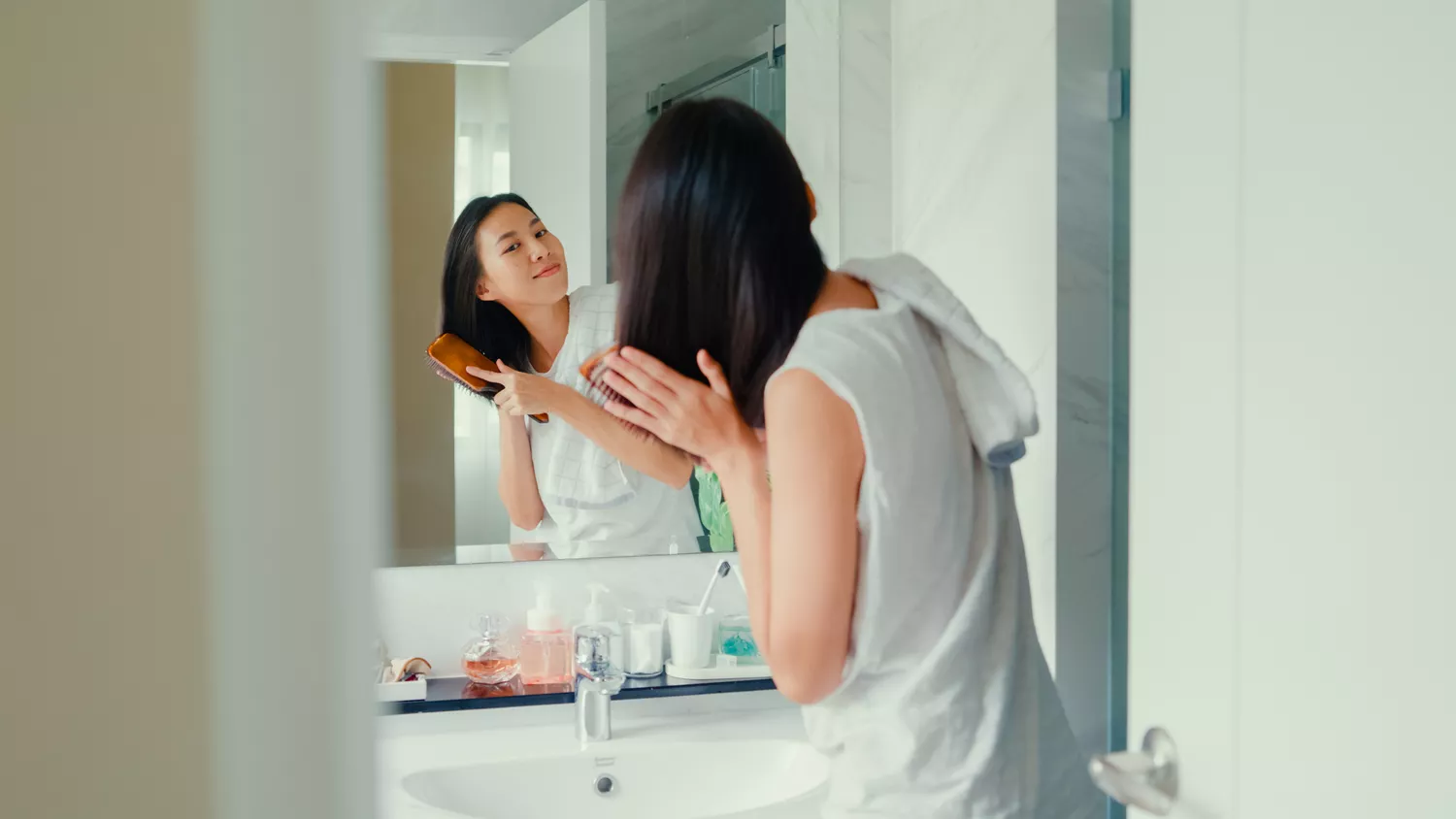 A person brushing their long, healthy hair in front of a bathroom mirror, showing sheen and strength.
