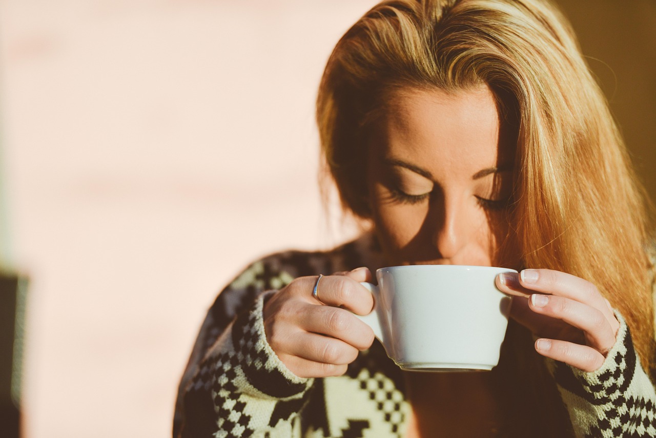 A person sitting peacefully by a window holding a steaming mug of latte