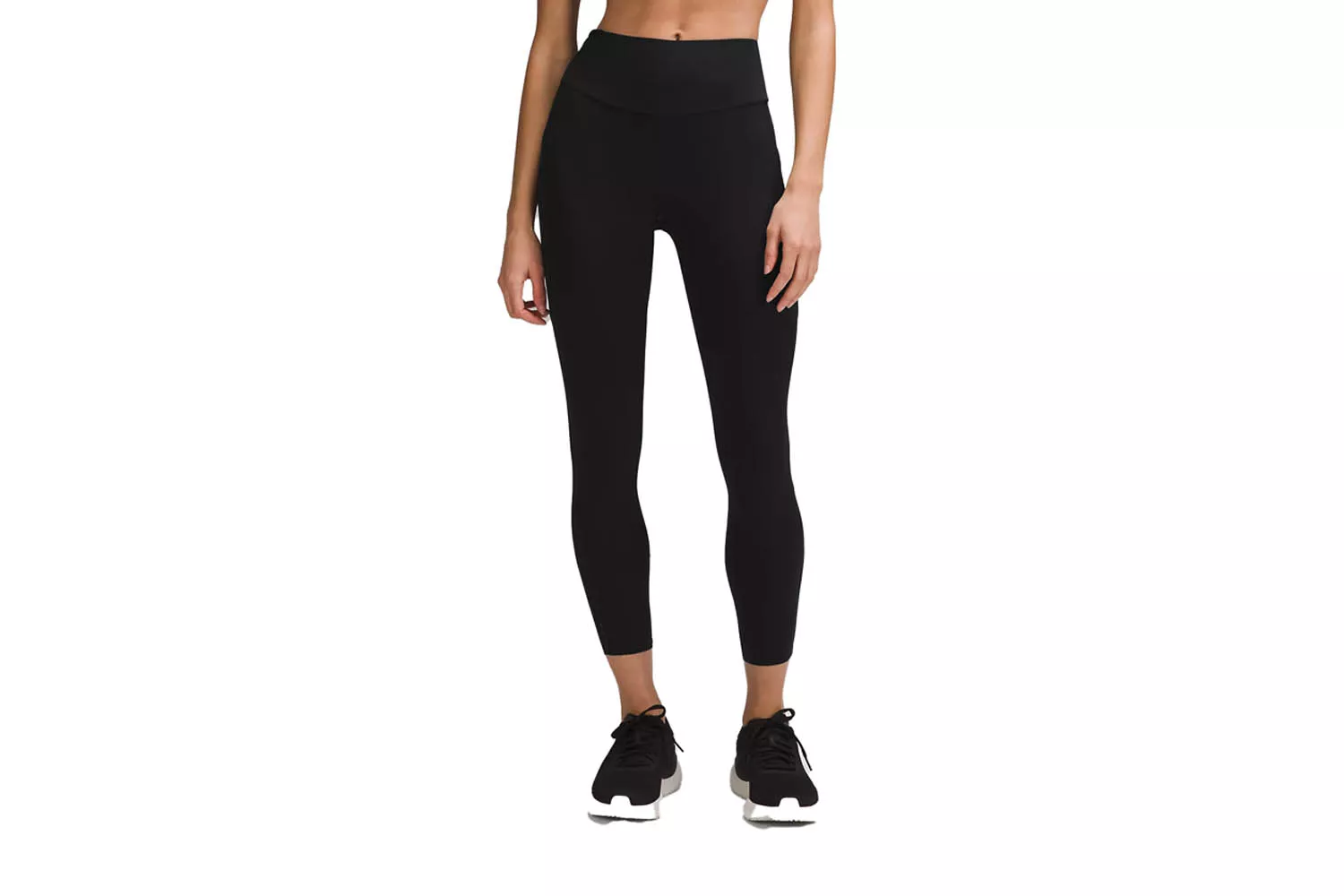 A woman standing in a neutral pose wearing high-rise petite athletic leggings and white sneakers.