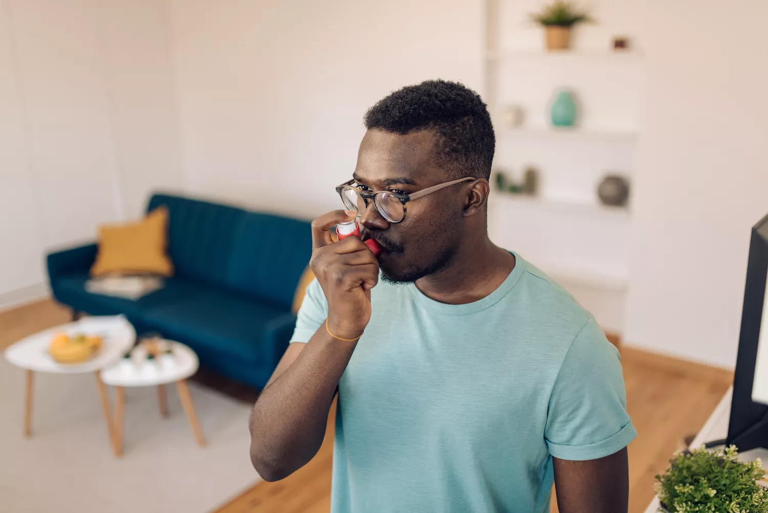 A man with glasses using a rescue inhaler in a domestic setting.