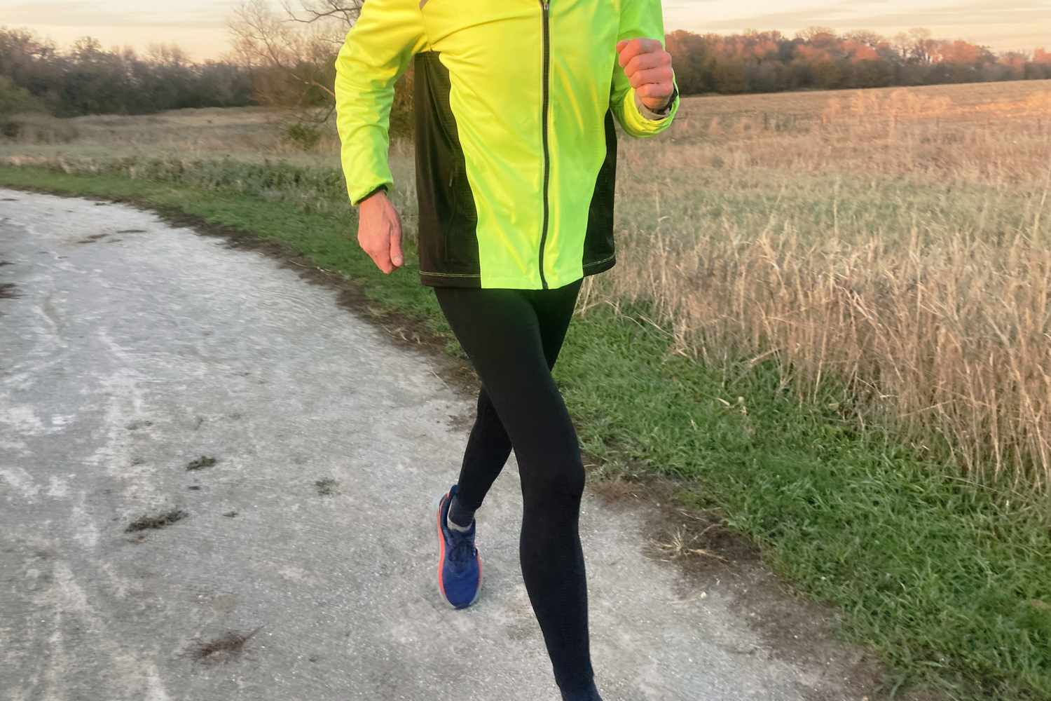 A person running on a rural path during golden hour wearing black leggings.