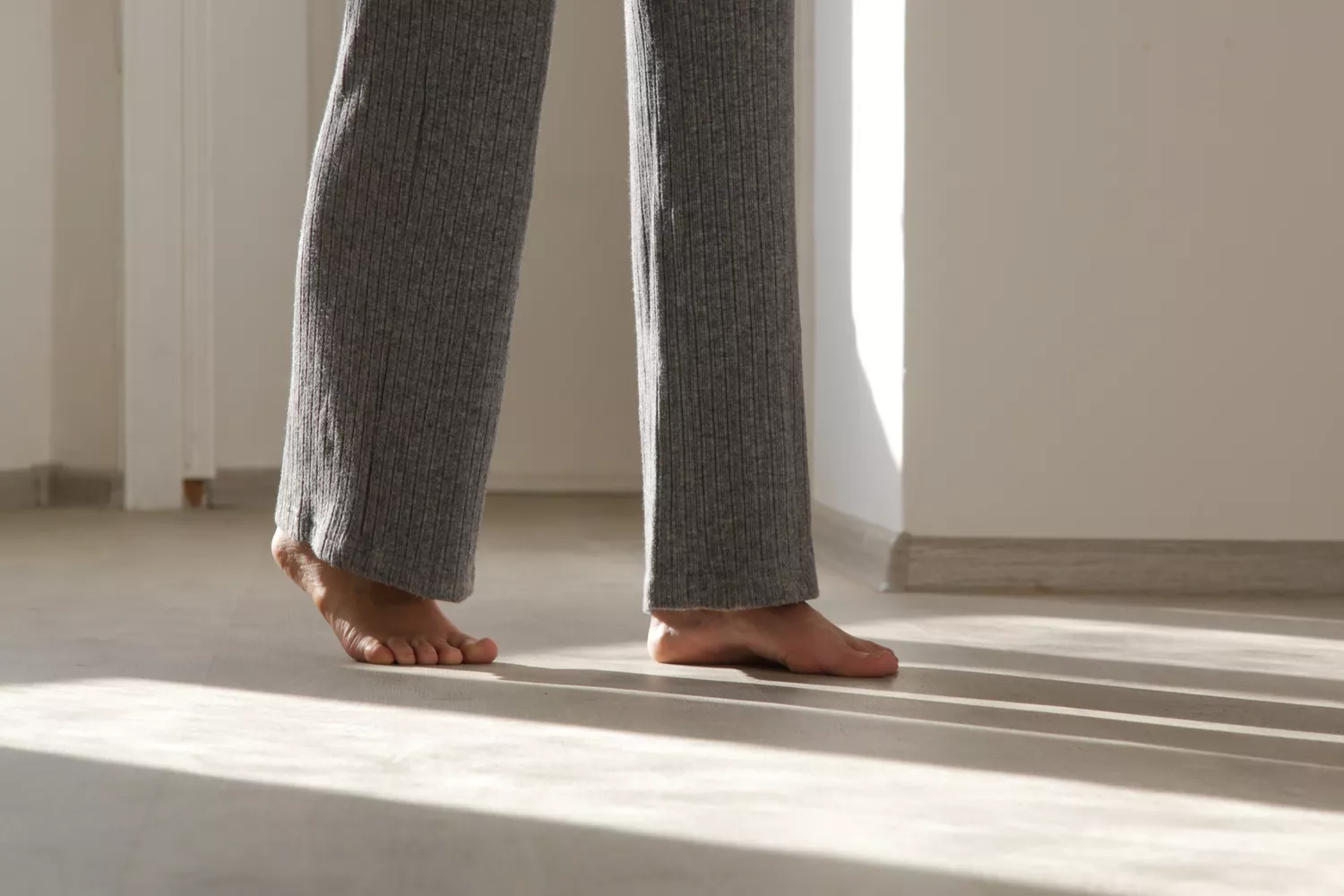 A person standing barefoot in a sunlit room, emphasizing a natural and grounded posture.