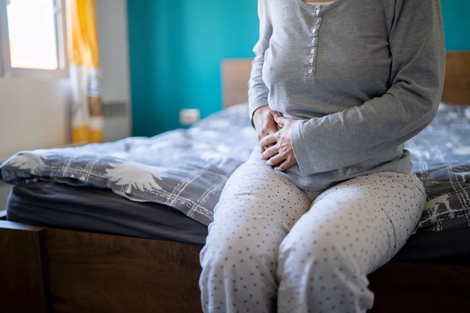 A person holding their stomach in pain while in bed, depicting physical symptoms that may occur alongside night sweats.