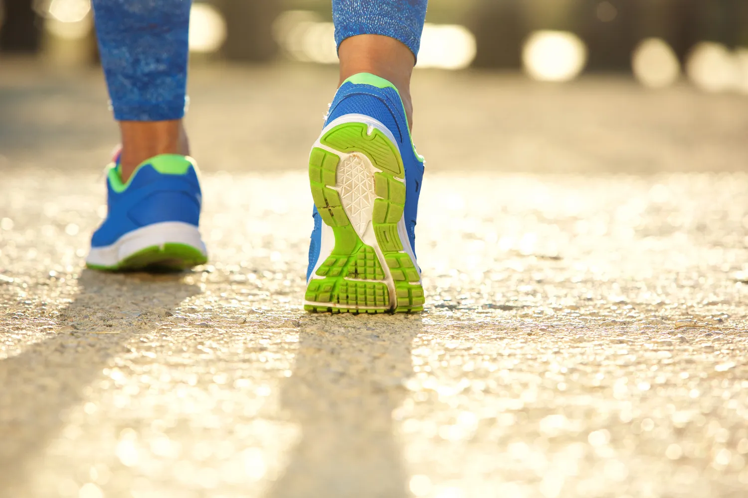 A close-up of a person's legs and feet walking on a paved pathway.