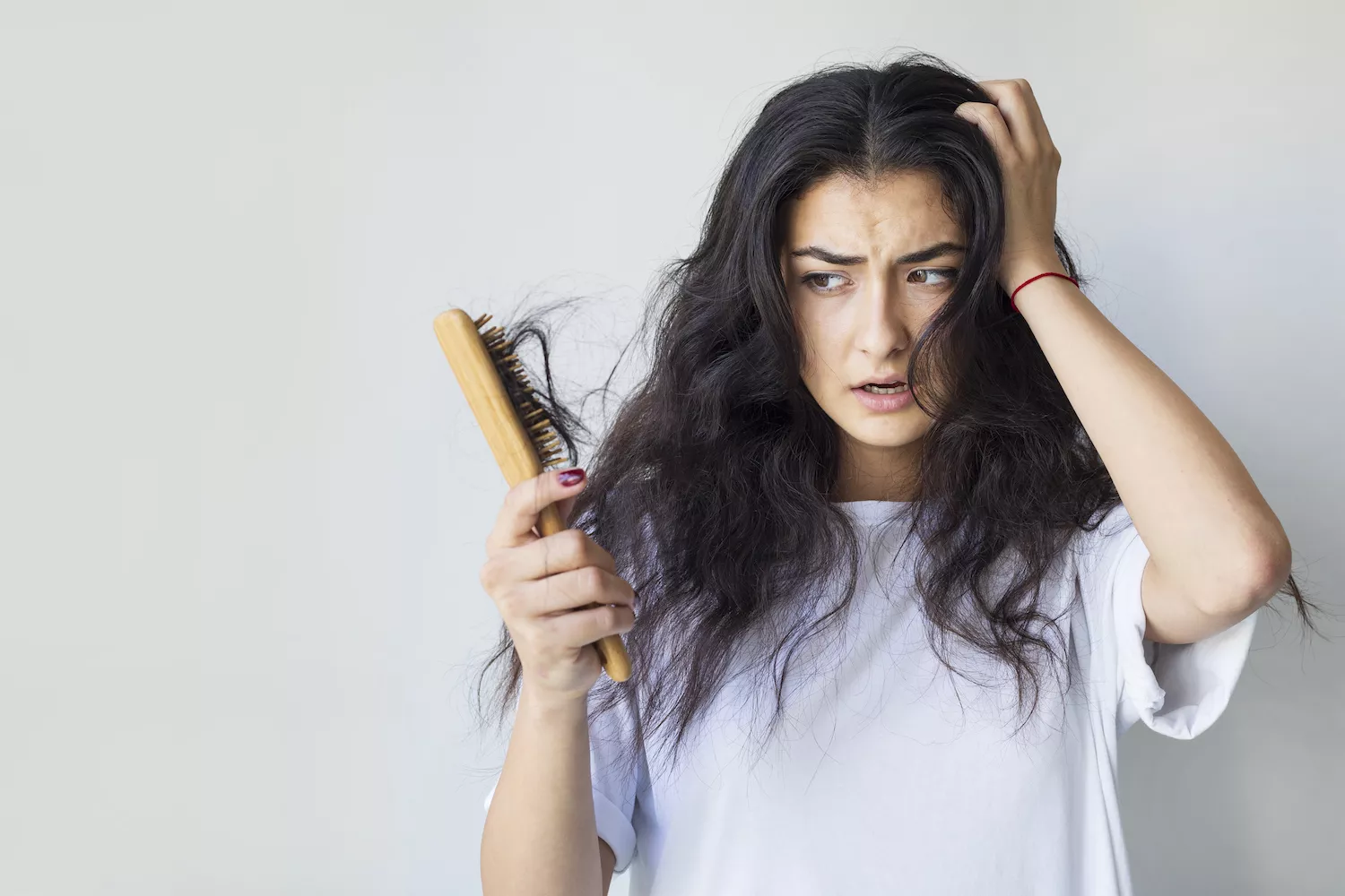 A woman looking concerned while examining hair on a brush, representing potential systemic symptoms of metabolic syndrome.