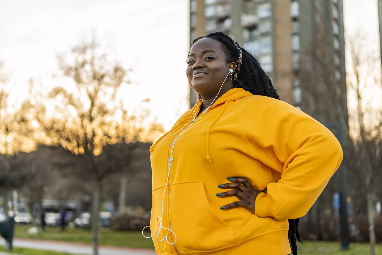 A smiling woman in fitness attire standing confidently in an urban park.
