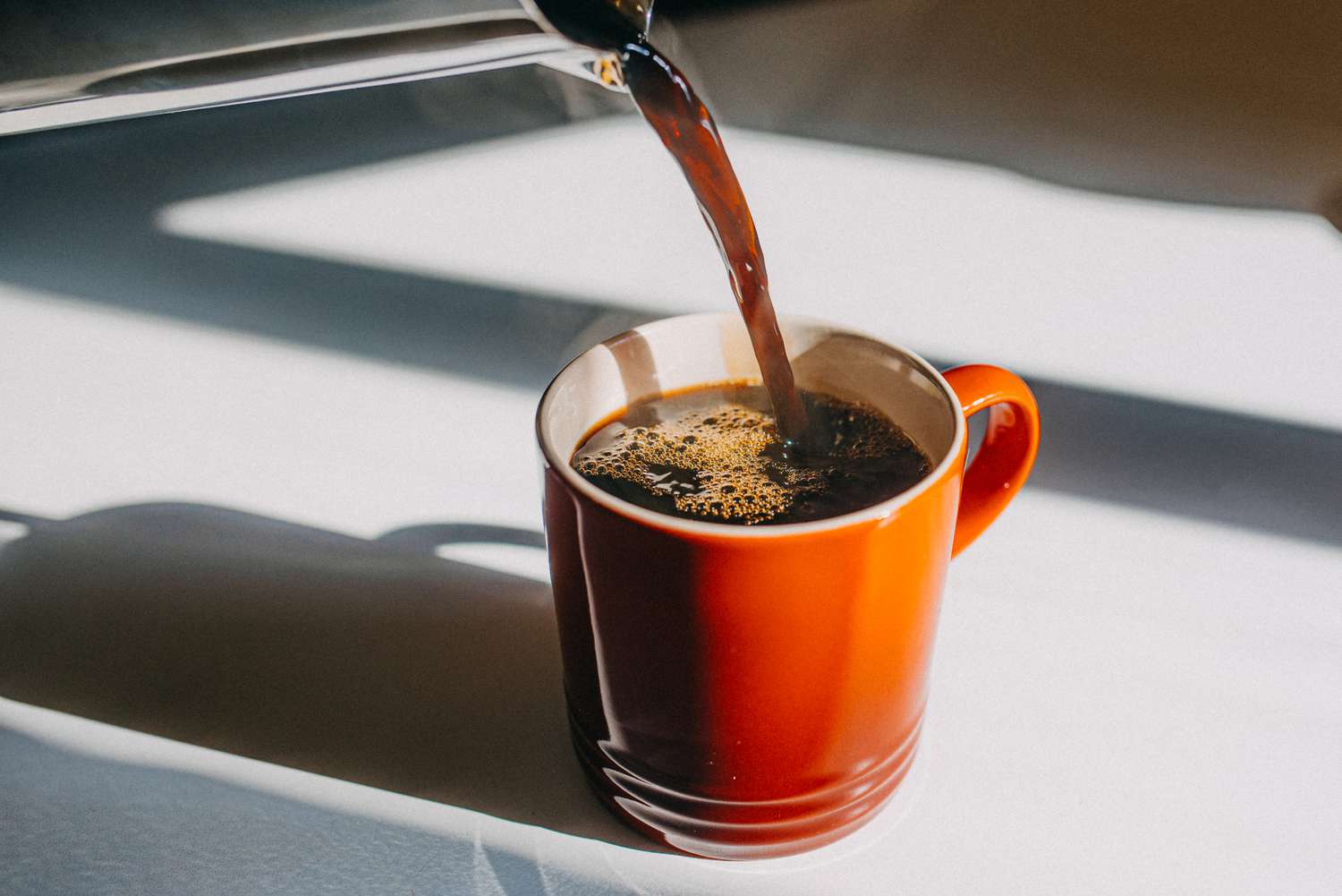 Coffee being poured into a ceramic mug on a wooden surface.