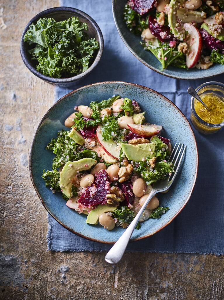 A top-down view of a fresh kale salad featuring winter seasonal produce and seeds.