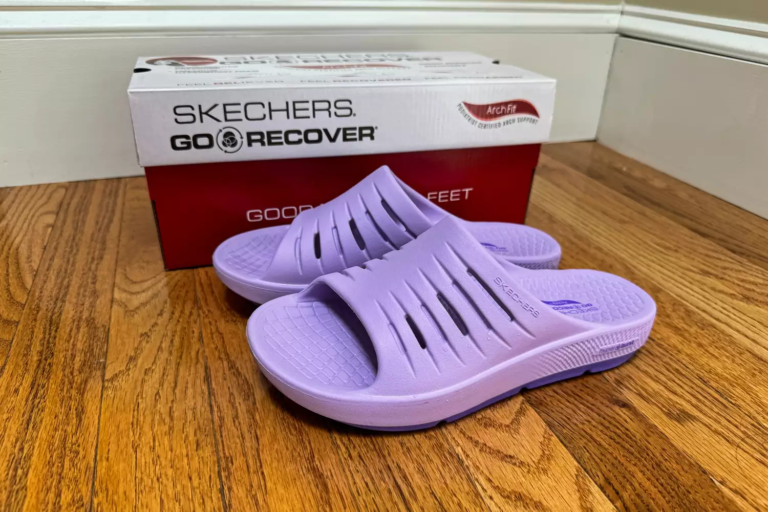 Lavender purple Skechers GO RECOVER slides with ArchFit technology shown with their original box on a wooden floor.