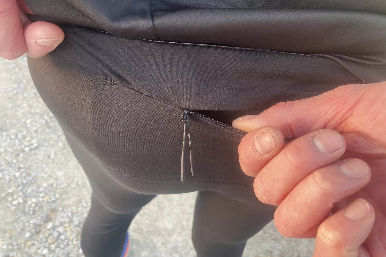 Close-up of a person's hand using a zipper on a side pocket of athletic leggings.